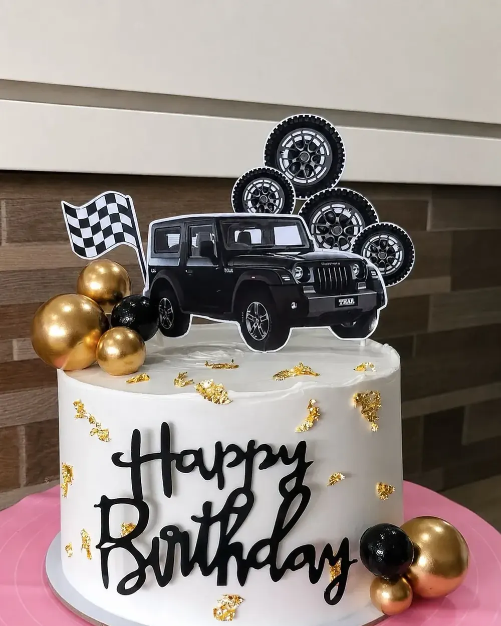 A bento cake with a Happy Birthday topper, a toy car and tire decorations